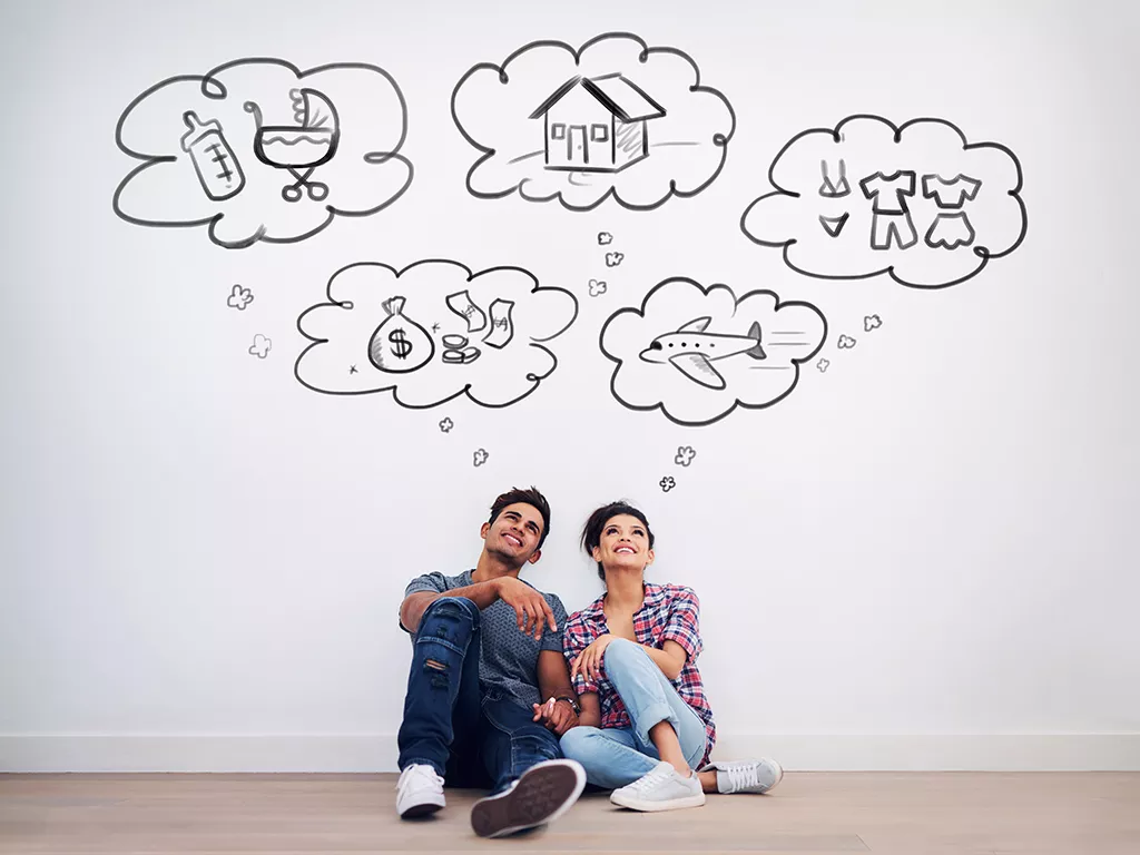 A couple with thought bubbles around their heads depicting a home, money, a baby, clothes, and an airplane