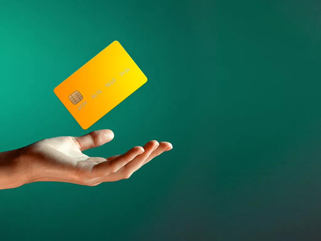 Hand reaching out with a yellow credit card floating above it on a green background