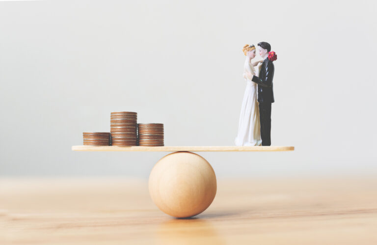 Wooden scale with marriage figures on one end - and coins on other. Financial balance in marriage concept.