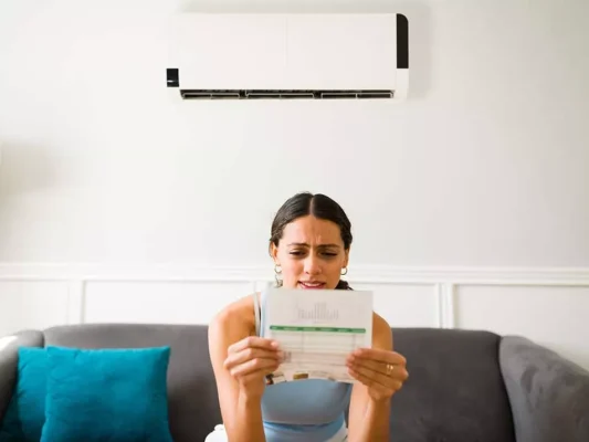 A woman sits on a couch holding a piece of paper and looking confused
