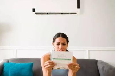 A woman sits on a couch holding a piece of paper and looking confused