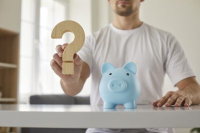 Man with piggy bank and wooden question mark.