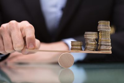Closeup of man balancing coins on a wooden balance beam