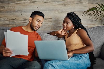 Shot of a young couple sitting in the living room at home and using a laptop to calculate their finances