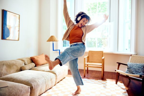 Cheerful woman in her 20s joyfully dancing in living room with arms out, kicking leg after becoming debt free