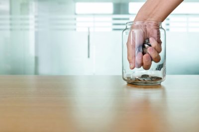 Hand grabbing coins from glass jar.