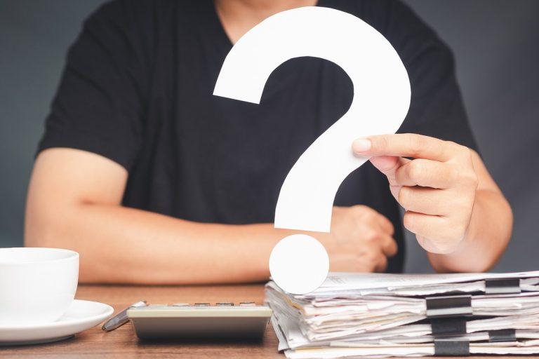 A young man in a black casual is holding a white question mark symbol while sitting at the table