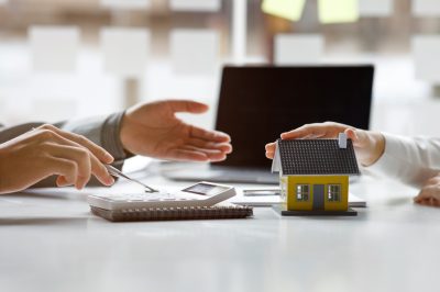 Man refinancing a home equity loan. Calculator and model home on table.