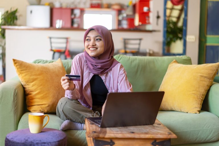 Woman on couch holding credit card near laptop