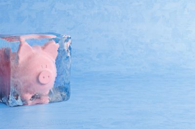 Pink piggy bank frozen in ice cube, frozen account concept, cold blue ice background