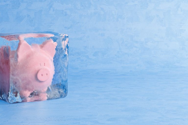 Pink piggy bank frozen in ice cube, frozen account concept, cold blue ice background