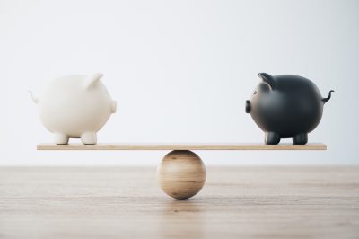White and Black Piggy Banks On Wooden Seesaw - Comparing financial options