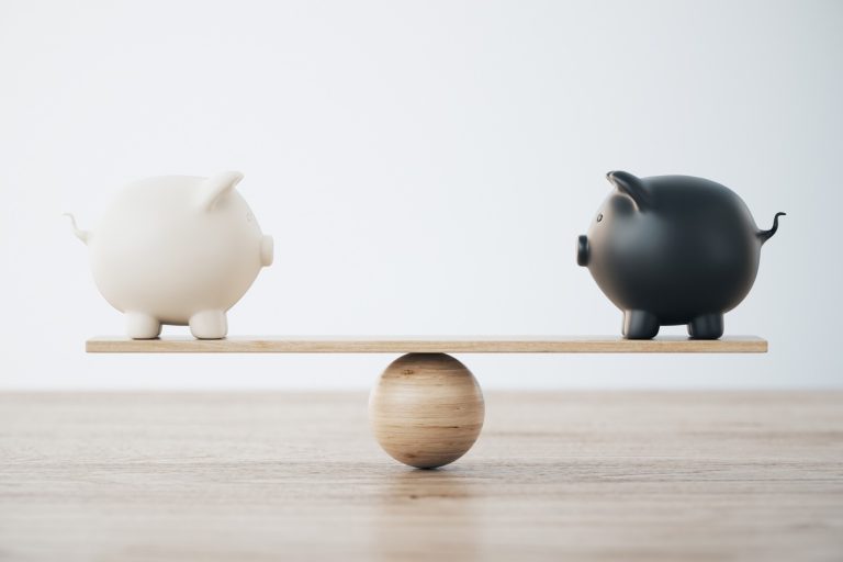White and Black Piggy Banks On Wooden Seesaw - Comparing financial options