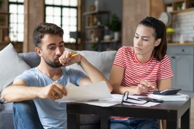 Frustrated concerned young couple calculating overspend budget, doing paperwork job at laptop, talking about financial problems, insurance, mortgage, fees, loan conditions, bankruptcy, economic inflation