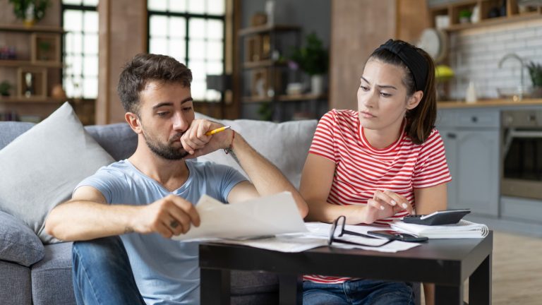 Frustrated concerned young couple calculating overspend budget, doing paperwork job at laptop, talking about financial problems, insurance, mortgage, fees, loan conditions, bankruptcy, economic inflation