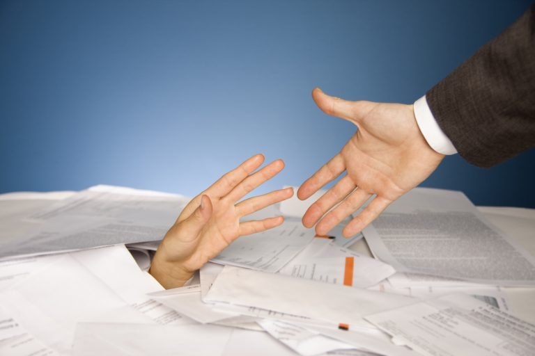 Hand reaching out from a pile of bills looking for help with finances