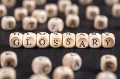 Glossary - word from wooden blocks with letters, alphabetical list with words meanings dictionary glossary concept, random letters around, top view on grey background