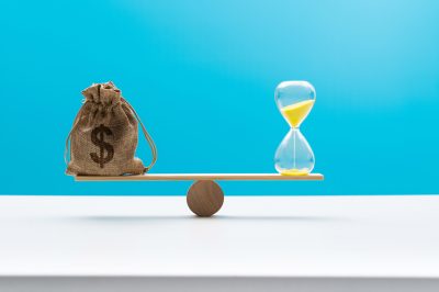 Wooden seesaw with money bag and hourglass