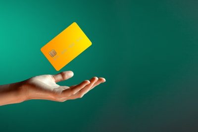 Hand reaching out with a yellow credit card floating above it on a green background