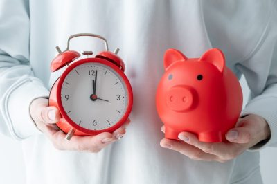 A person holding a red piggy bank and a red alarm clock