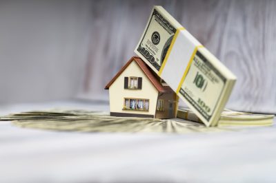 Figurine house with us money laying on top. Home equity concept