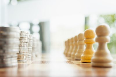 Symbolic image of stacked coins facing wooden chess pawns on a chessboard. Concept of economic power, financial strategy, workforce value, money
