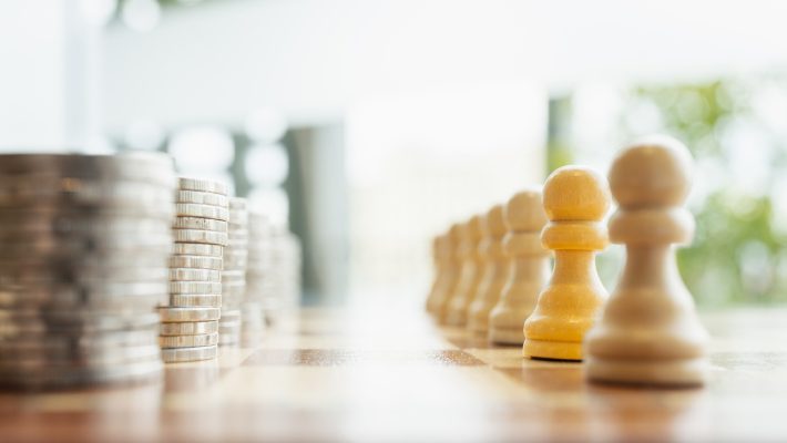Symbolic image of stacked coins facing wooden chess pawns on a chessboard. Concept of economic power, financial strategy, workforce value, money