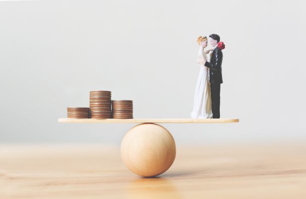 Wooden scale with marriage figures on one end - and coins on other. Financial balance in marriage concept.