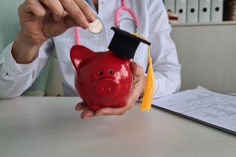 Doctor sitting at table and putting coin in piggy bank. Medical education development and training