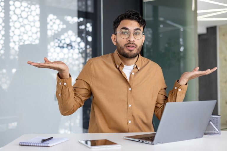 Young man with hands out looking confused at computer