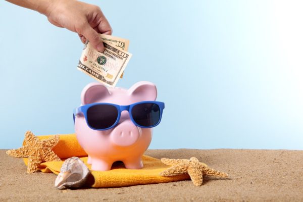 Pink piggy bank with beach items and money being put in