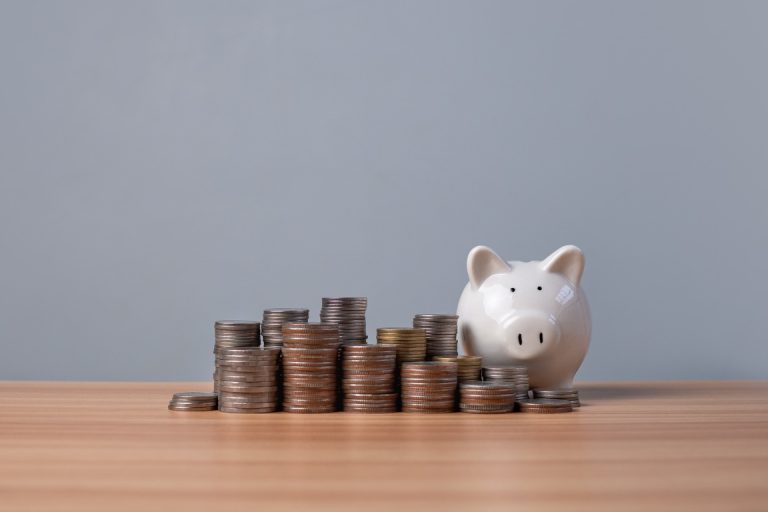 Piggy bank and coins lined up on a wooden floor with a white background. Concepts of finance, savings and investment.