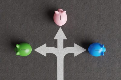 White divided road sign mark on asphalt with 3 different colored piggy banks going to different directions.