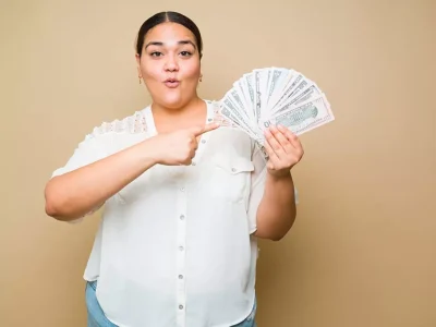 Woman making a sassy face points to a fan of cash in her other hand