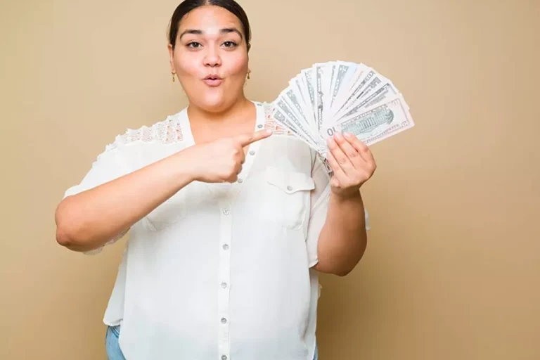 Woman making a sassy face points to a fan of cash in her other hand